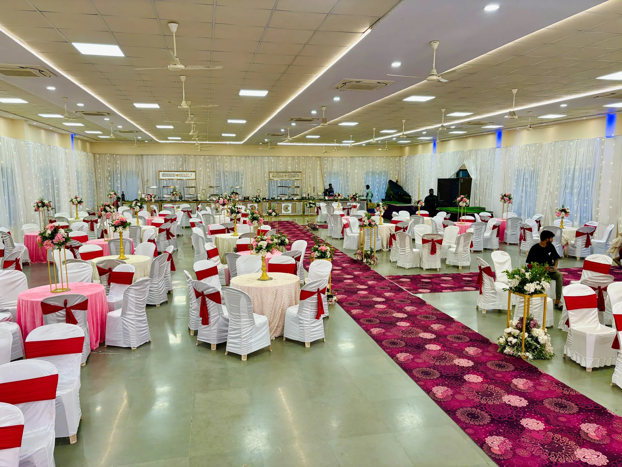 Banquet setup with round tables, floral stands and a red aisle at Yeshwant Hall